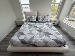A bed with a geometric patterned bedspread, two bedside tables, and a window with a view of trees.