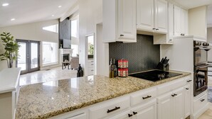 Une cuisine moderne avec des meubles blancs, des comptoirs en granit et un dosseret orné d’un motif en chevrons.