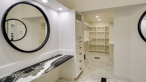 Une salle de bain dotée d’un comptoir en marbre, d’un grand miroir et d’un dressing avec des étagères.