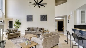Un vaste salon doté d’un haut plafond, d’un ventilateur de plafond moderne et d’un coin cuisine avec un dosseret en carreaux disposés en motif chevron.