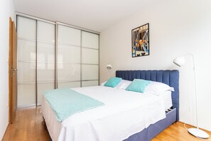 A bedroom with a bed, a blue headboard, a white wall, a floor lamp, and a sliding glass door.