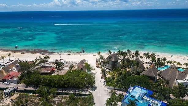 A beach resort with thatched-roof huts, a swimming pool, and a view of the ocean. - Beautiful 2bd-2bth - Ocean Views (Playa del Carmen)