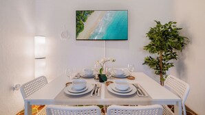 Un comedor con una mesa dispuesta para dos, una planta en maceta y un cuadro con una playa.