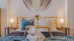 Una cama bien tendida con un edredón azul, una toalla blanca y una bandeja con un vaso de agua y un florero con flores.