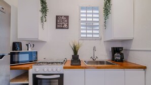 Una cocina compacta con gabinetes blancos, microondas, estufa y cafetera.