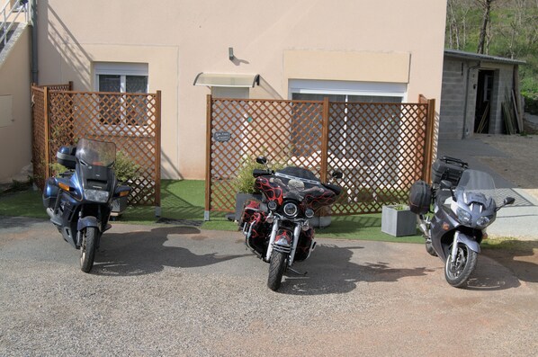 Trois motos sont garées devant un immeuble dont l’entrée est fermée par un portail.