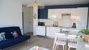 A modern kitchen with white cabinets, a microwave, and a coffee maker. There is a dining area with a white table and chairs.