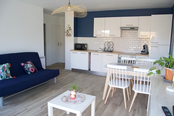 A modern kitchen with white cabinets, a microwave, and a coffee maker. There is a dining area with a white table and chairs.