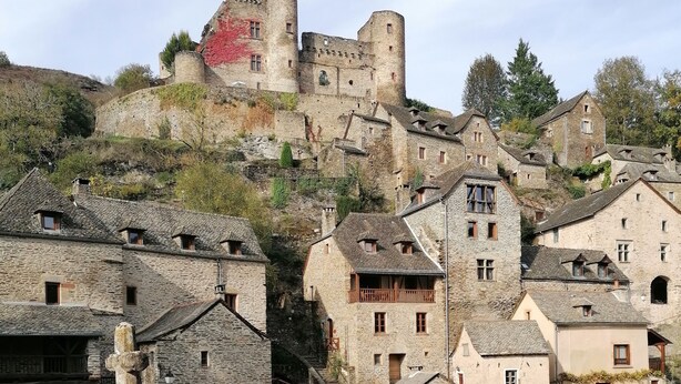 A historic stone castle atop a hill with traditional stone buildings below.