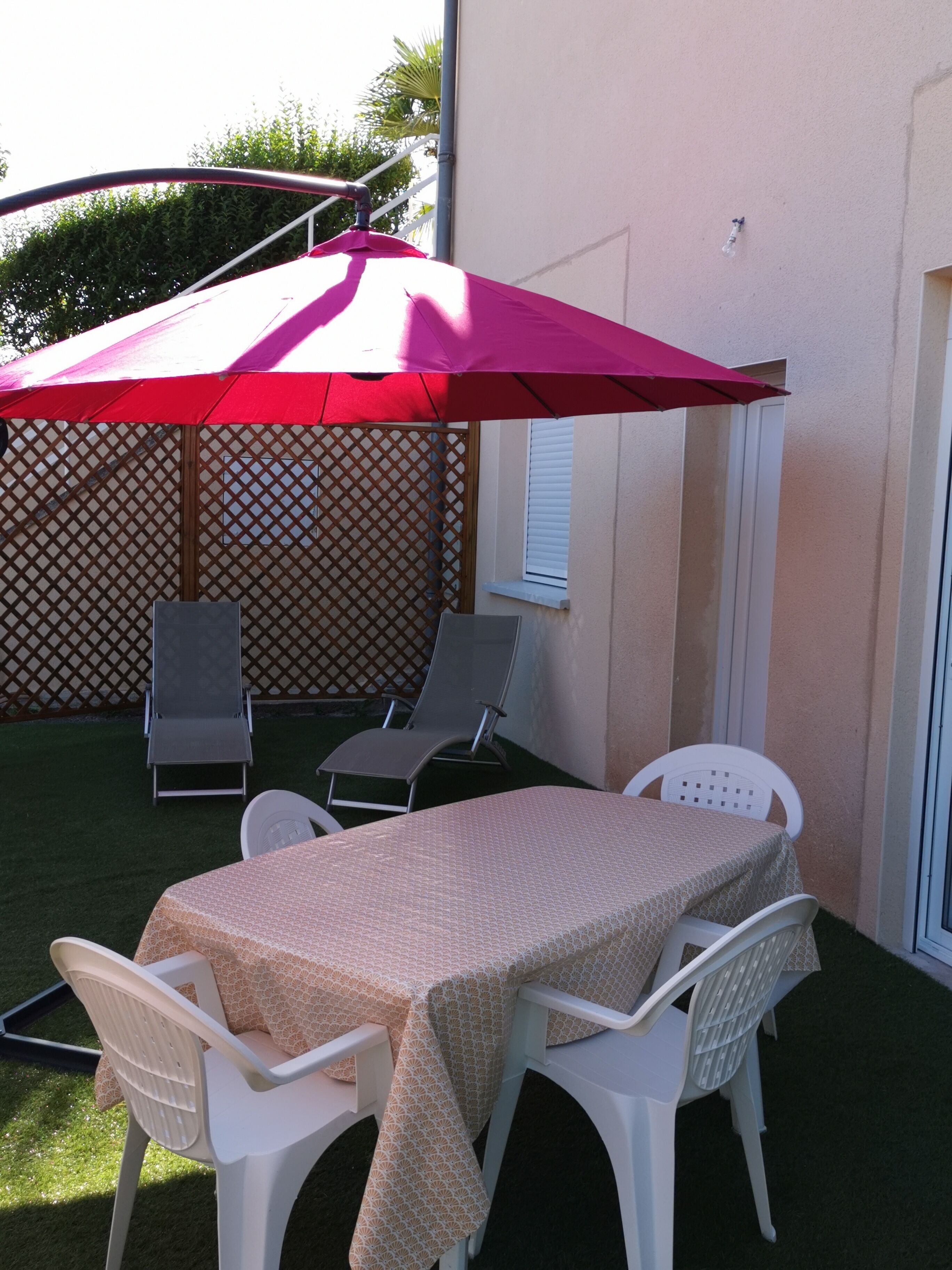 Un patio al aire libre con una mesa y sillas, un paraguas rojo y un cerco de madera.