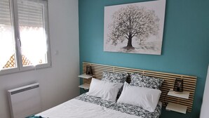 A bedroom with a bed, a window, a wall-mounted lamp, and a painting of a tree.