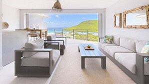 Una sala de estar moderna con un amplio ventanal que ofrece una vista panorámica del océano y una colina.