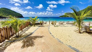 Un chemin pavé mène à une plage bordée de palmiers et parsemée de chaises de plage.