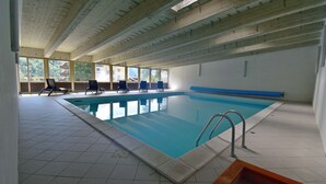An indoor swimming pool with clear blue water, tiled floor, and wooden ceiling beams. - Presanella Home 4 MhD (Madonna di Campiglio)