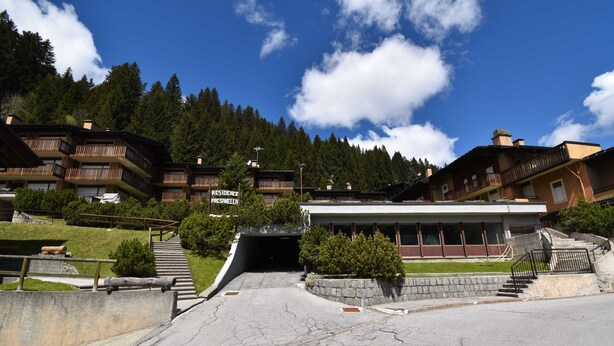 A hotel entrance with a stone pathway leading to a building with multiple balconies and a mountain backdrop. - Presanella Home 4 MhD (Madonna di Campiglio)