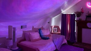 Une chambre avec un plafond en pente, un lit, une table de chevet, une lampe et une horloge fixée au mur.