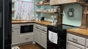 Une cuisine compacte avec des meubles blancs, une cuisinière noire et des étagères en bois au-dessus du plan de travail.