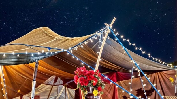 Een tent met een sterrenhemel, een tafel met een bloevas, en kleurrijke textielen op de grond.