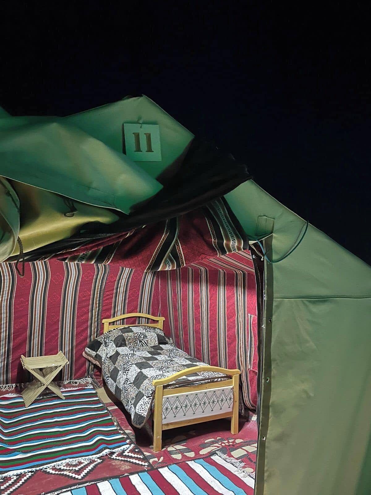 A tent with a bed, a small table, and a striped rug.