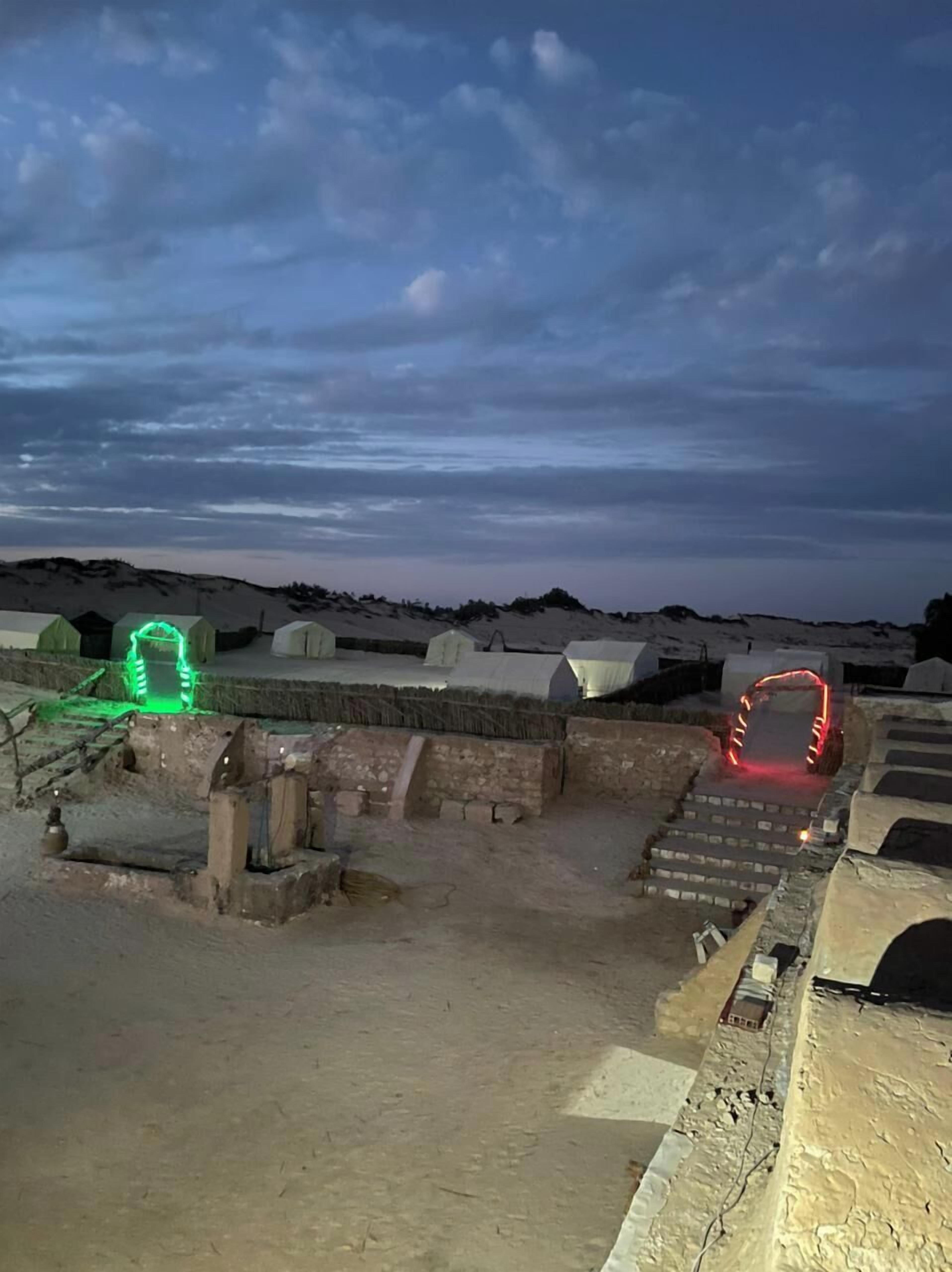 A rooftop with a view of the sky and distant landscape, featuring several illuminated structures.