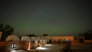 Een sterrenhemel boven een traditioneel dorp met rieten hutten en een open ruimte in het midden.