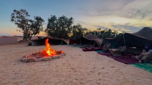 Een camping met tenten, een vuurplaats en mensen die op matten zitten.