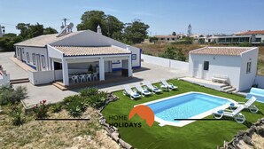 Une villa moderne dotée d’un patio couvert, d’une piscine et d’une pelouse bien entretenue.