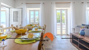 Un espace de repas lumineux, avec une table mise pour le petit-déjeuner, comprenant des croissants et du jus d’orange, et un canapé agrémenté d’un vase de fleurs en arrière-plan.