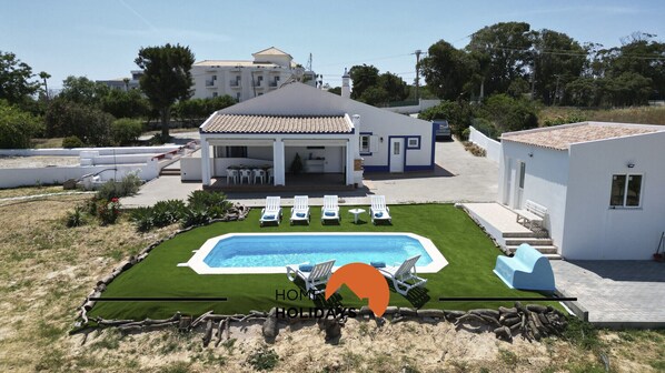 A modern villa with a swimming pool, outdoor seating, and a well-maintained lawn.