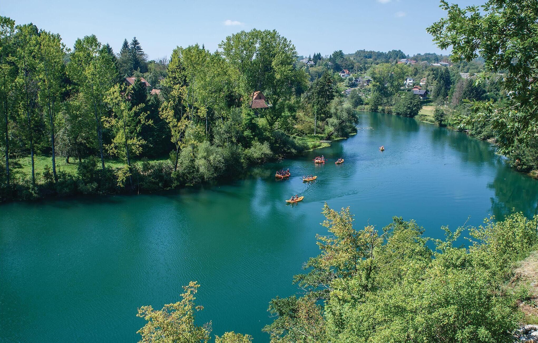 Ein Fluss, umgeben von dichtem Grün und Häusern im Hintergrund.