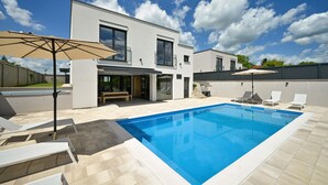 Ein modernes, zweistöckiges Haus mit Swimmingpool, Sitzgelegenheiten im Freien und einer überdachten Terrasse.