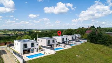 A modern residential complex with multiple houses, a swimming pool, and a scenic view of the countryside.