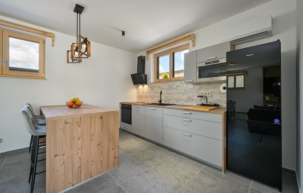 Una cocina moderna con una isla de madera, un refrigerador negro y un ventanal con vista a follaje.