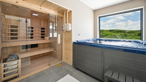 Un sauna avec des bancs en bois, un espace douche fermé par des parois de verre et une grande fenêtre donnant sur la verdure.