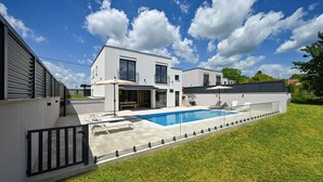 Une maison moderne à deux étages, dotée d’une piscine, d’un patio couvert et d’une cour clôturée.