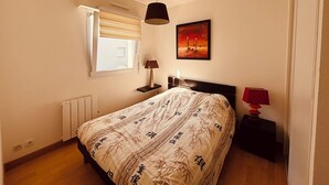 Un dormitorio con cama, mesita de noche, lámpara, ventana con persianas y un cuadro en la pared.