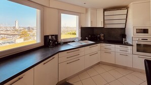 Una cocina moderna con armarios blancos, encimera negra y vistas a la ciudad a través de amplios ventanales.