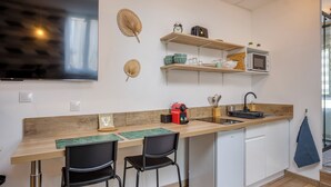 Una cocina moderna con encimera de madera, dos taburetes negros, un microondas integrado y un estante pequeño con utensilios de cocina.