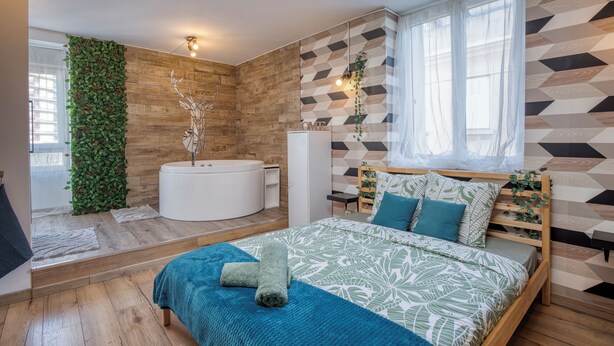Un dormitorio moderno con cama, bañera integrada y un amplio ventanal con cortinas translúcidas.