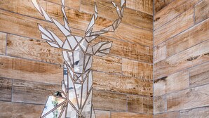 Un baño con pared de madera, un espejo con diseño de cabeza de ciervo y una encimera blanca con grifo y dispensador de jabón.