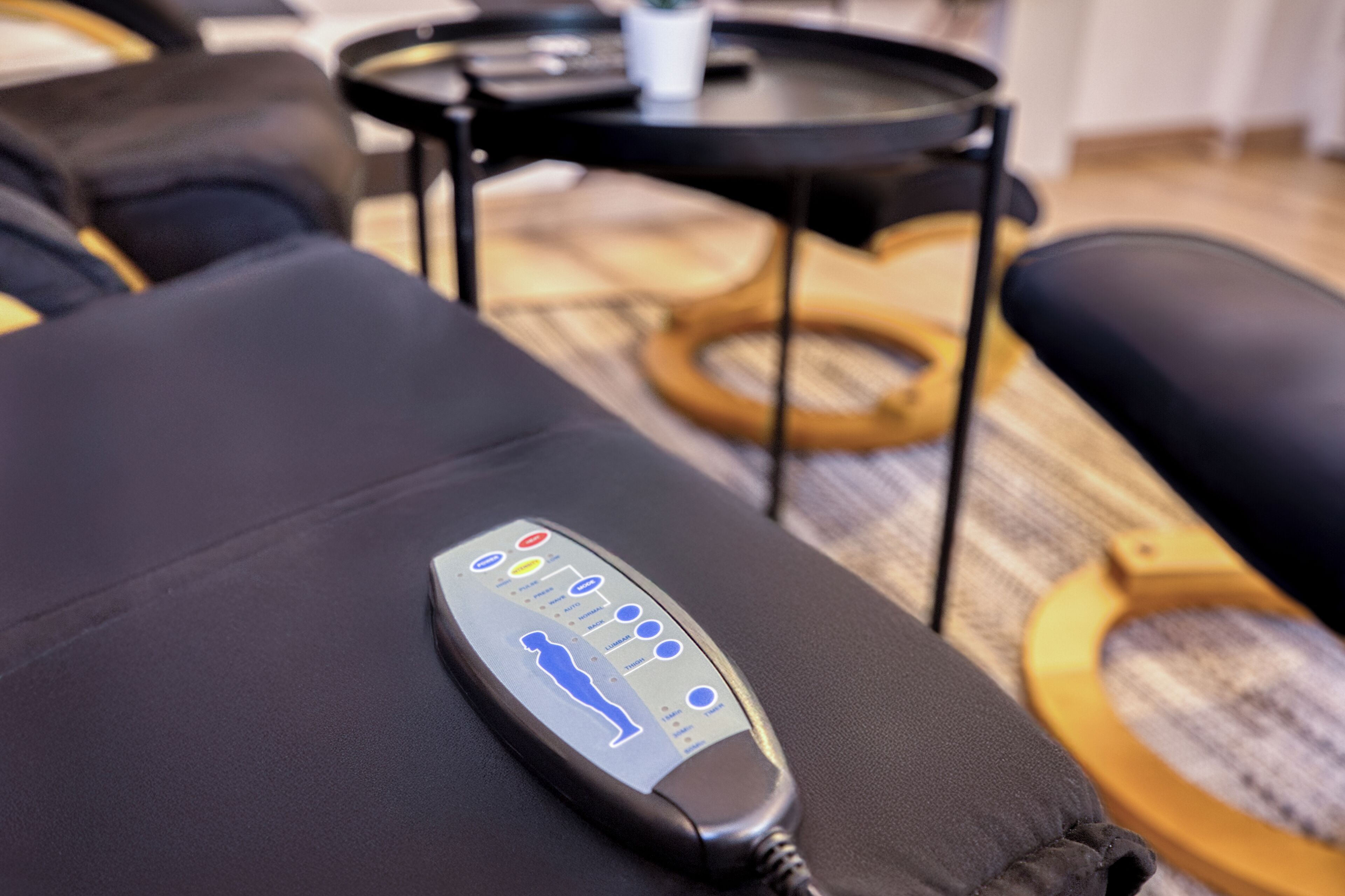 A massage chair with a control panel, a small table, and a wooden floor.