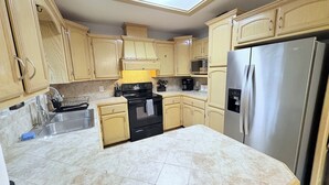 A kitchen with wooden cabinets, a stainless steel refrigerator, a black stove, a microwave, and a skylight.