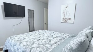 A bedroom with a bed, a television on the wall, a door, and a painting.