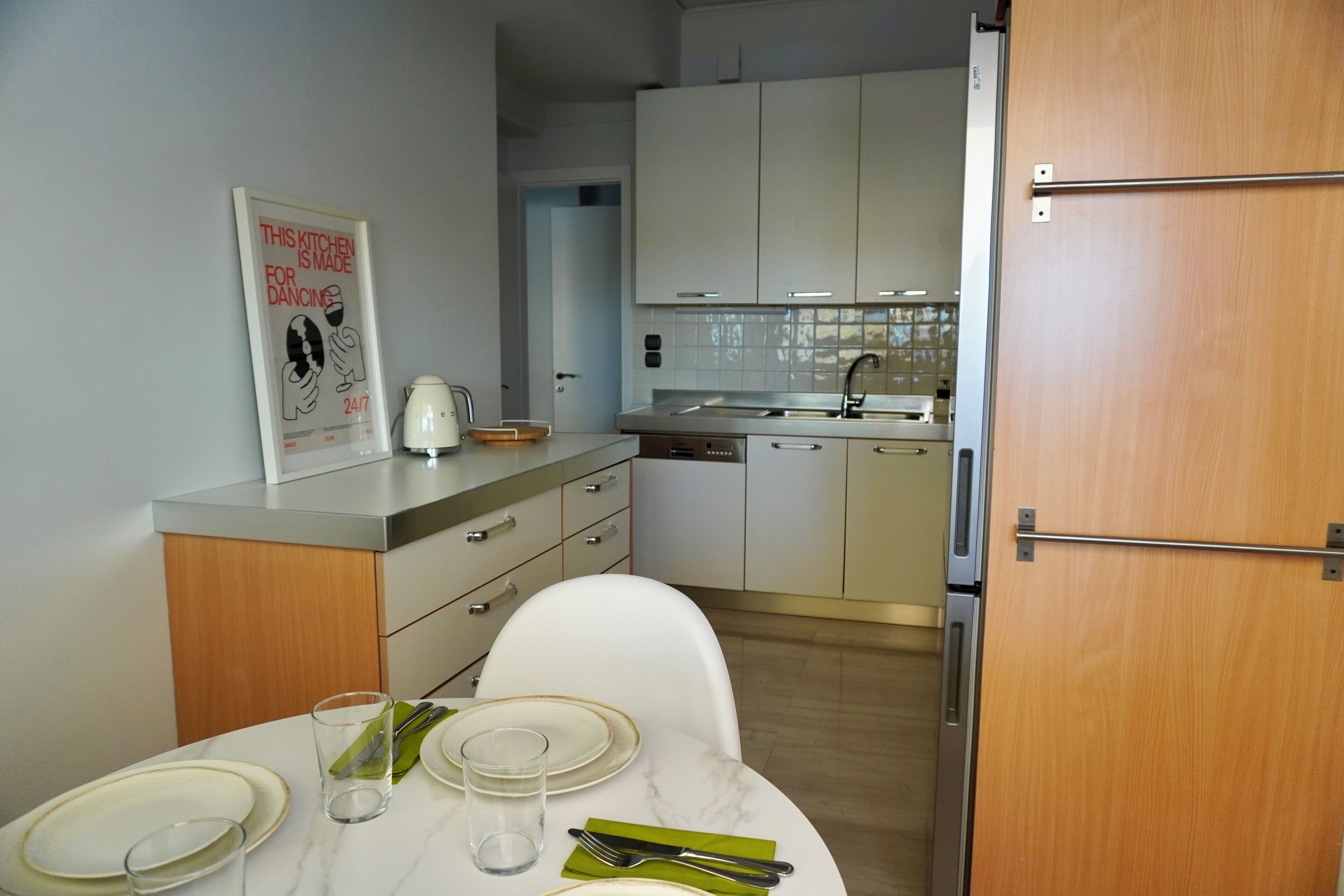 Una cocina moderna con armarios blancos, una mesa de comedor para dos personas y un cartel en la pared.