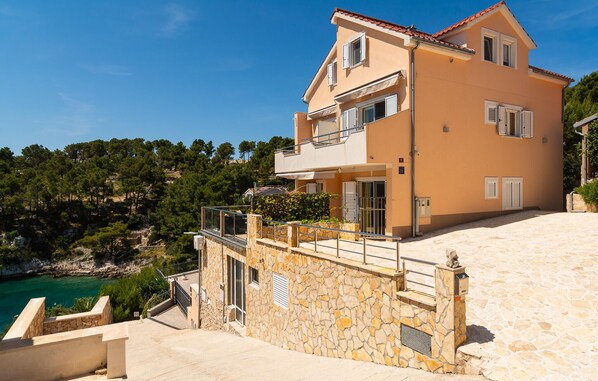 A two-story house with a stone facade, a balcony, and a view of the sea.