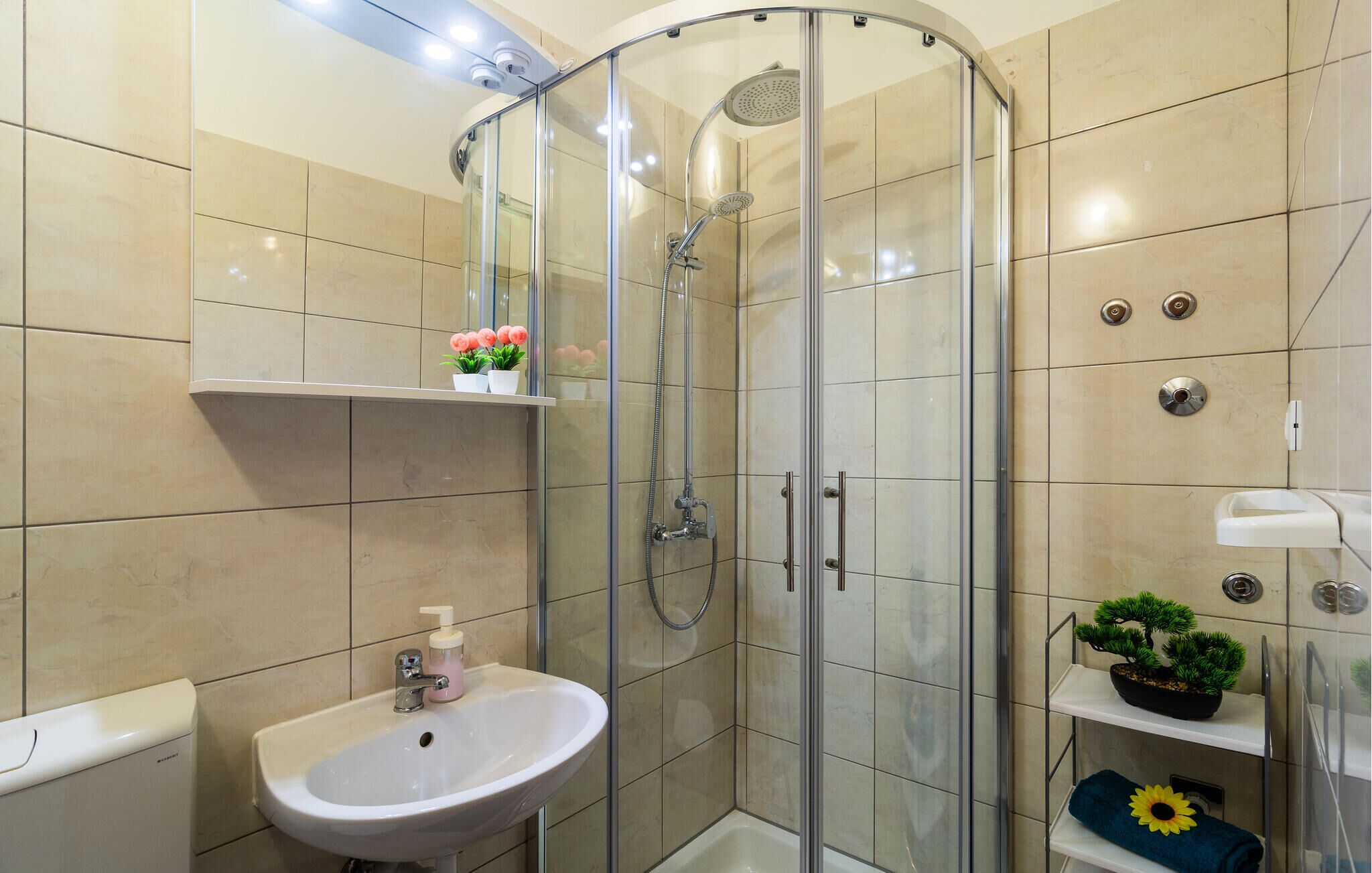 A modern bathroom with a glass-enclosed shower, a white sink, and a shelf with decorative items.