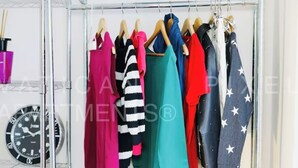 A clothing rack with various garments including a red dress, a black and white striped sweater, and a denim jacket with star patterns. - Vatican Pixel Apartments - DOUBLE (Unknown)