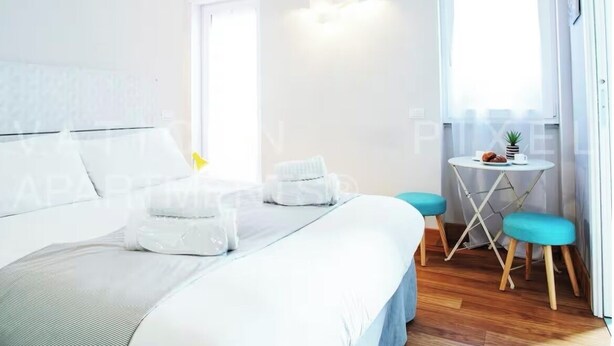 A modern hotel room with a large bed, a small round table, and two blue chairs. - Vatican Pixel Apartments - DOUBLE (Unknown)