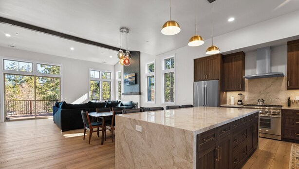 Une cuisine moderne dotée d’un grand îlot central, de meubles en bois foncé, d’appareils électroménagers en acier inoxydable et de luminaires suspendus.