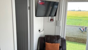 A room with a leather chair, a mounted TV, and a view of a green field through a window. - Seaside Chalet Escape in Bridlington (Bridlington)